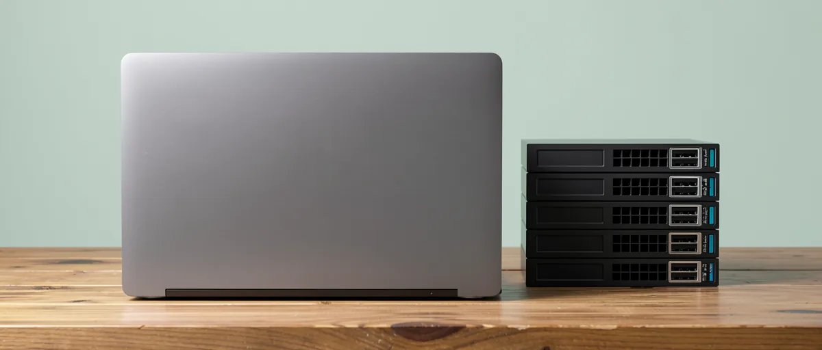 A closed laptop beside a stack of external hard drives on a wooden desk — illustration for Best Backup Software for Windows in 2026