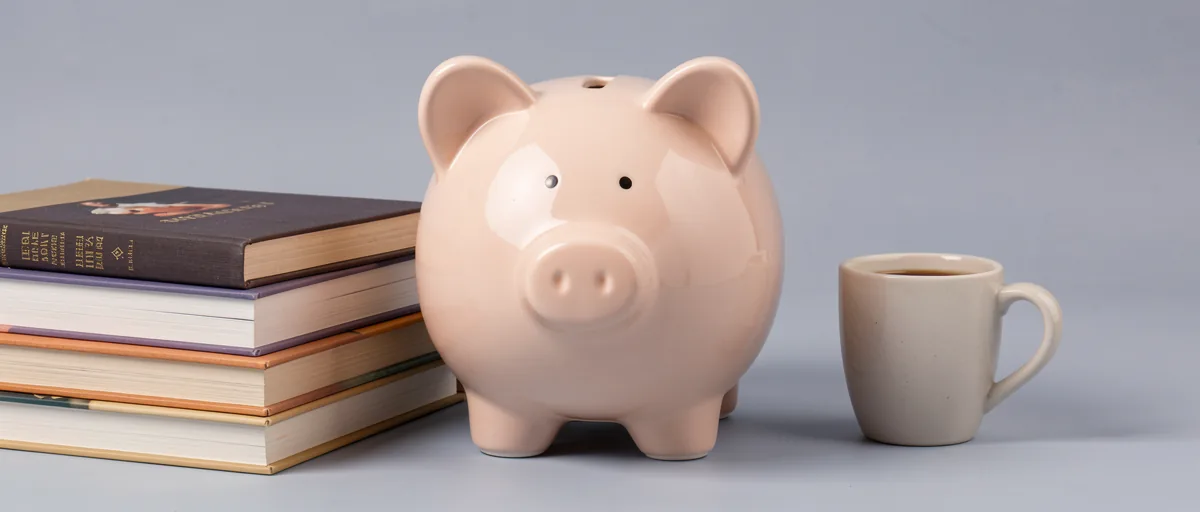 A ceramic piggy bank beside a stack of textbooks and a coffee mug — illustration for Best Budgeting App for College Students in 2026