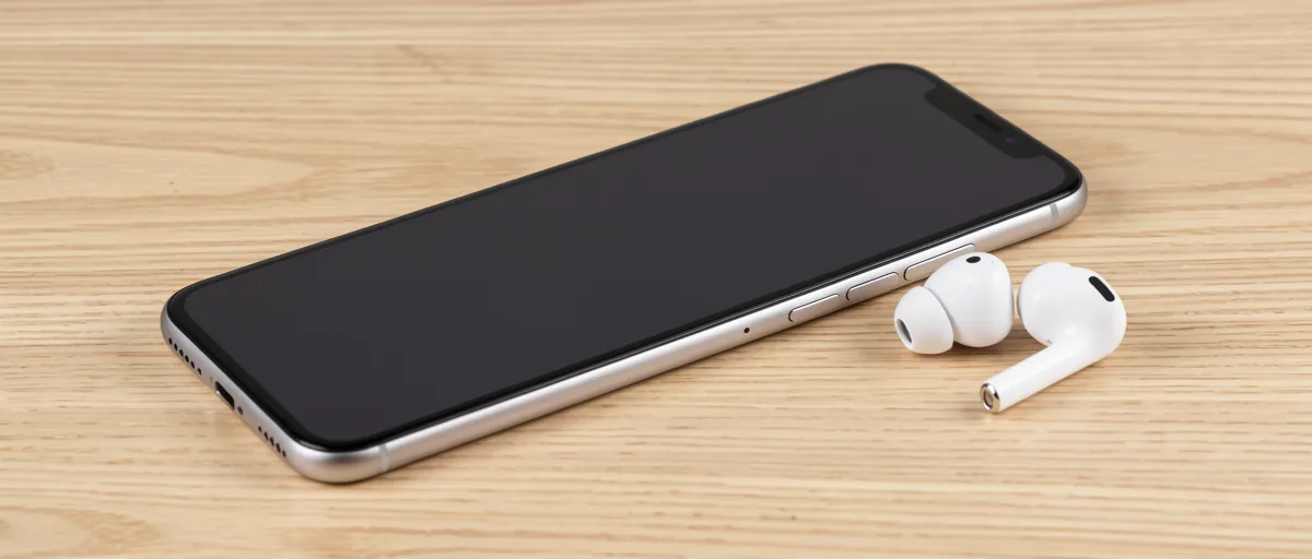 A smartphone lying face down on a light oak desk beside white wireless earbuds — illustration for Best Scanner App for Iphone Free in 2026